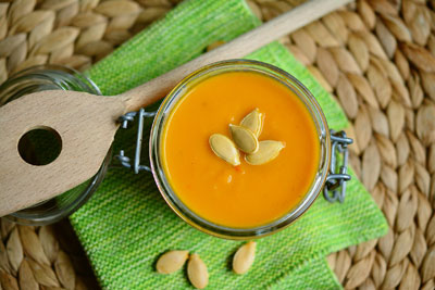 Photo of a jar of pumpkin soup on a green placemat with wooden spoon.